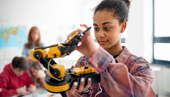 College student holding a robotic project in a classroom.